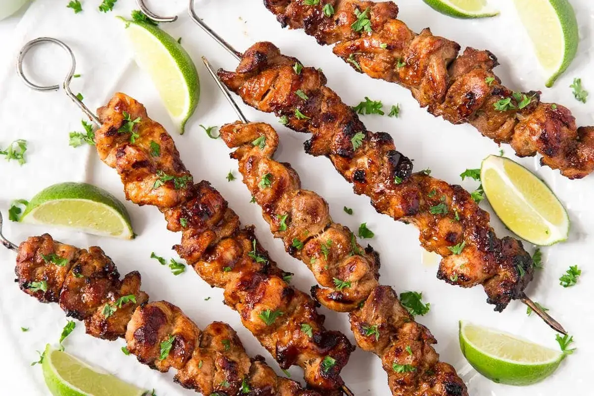 Brochettes de poulet grillées, garnies de persil frais et accompagnées de quartiers de citron vert. Un délice estival !