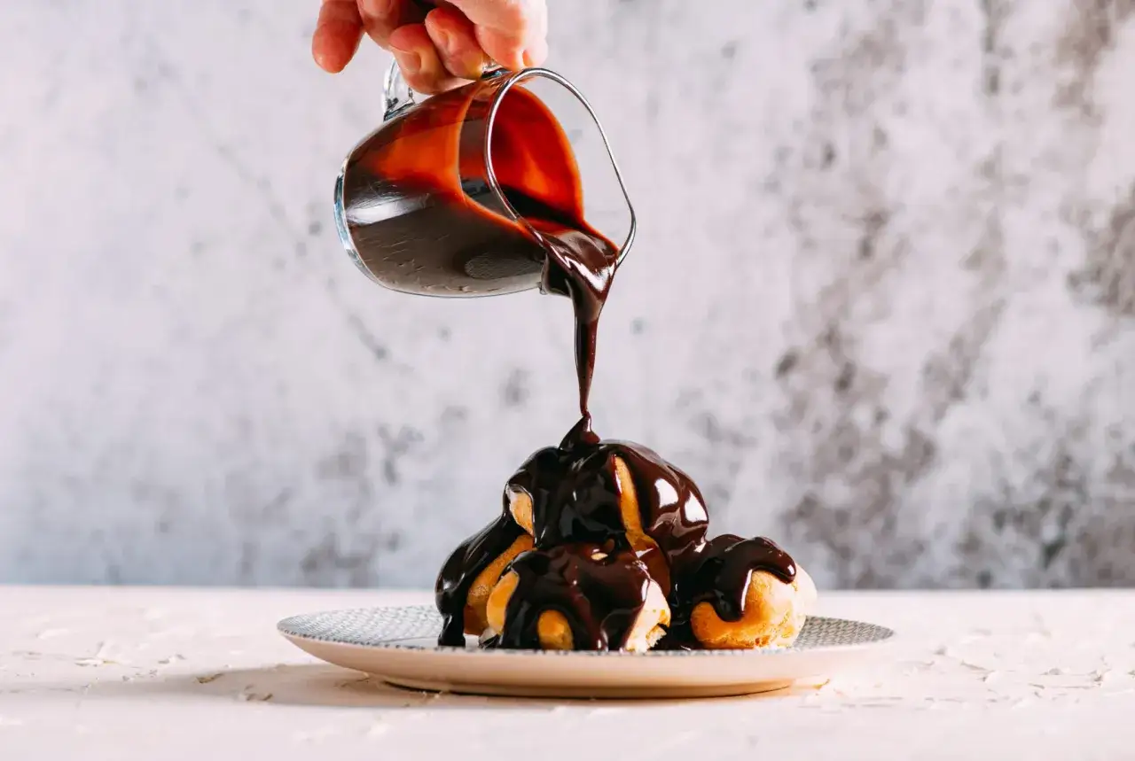 Sauce au chocolat versée sur des profiteroles. Une étape clé de la recette profiteroles au chocolat pour un dessert gourmand.