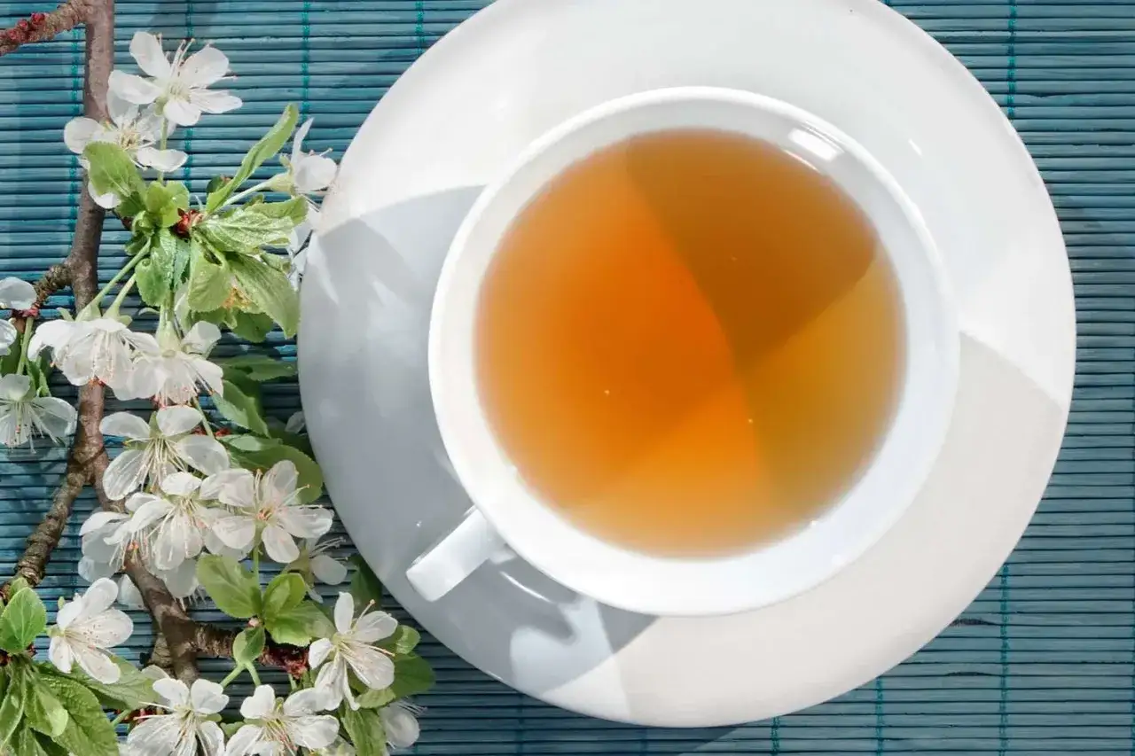Tazza di t&egrave; ambrato accanto a rami fioriti. Nonostante la sua apparenza rilassante, la camomilla fa male al cuore se consumata in eccesso.