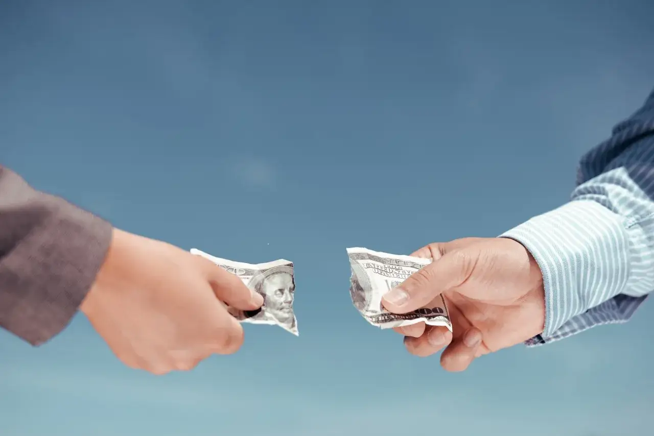 Rozdzielność majątkowa a kredyt: dwie ręce rozrywają banknot 100 dolarów.