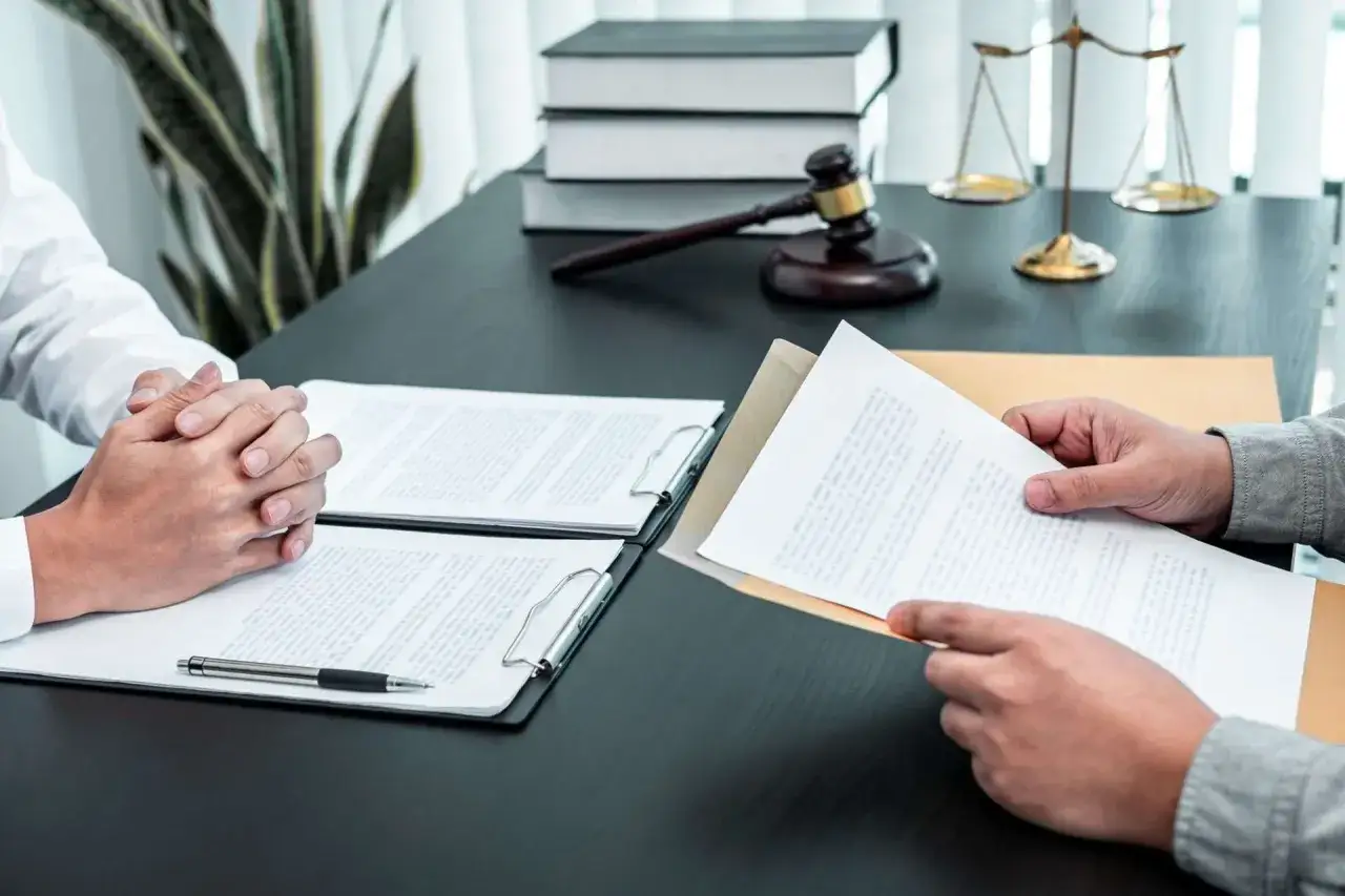 Deux mains se font face autour de documents juridiques. La balance de la justice et un maillet sont visibles en arri&egrave;re-plan, symbolisant les inconv&eacute;nients potentiels d'une communaut&eacute; universelle mal g&eacute;r&eacute;e.