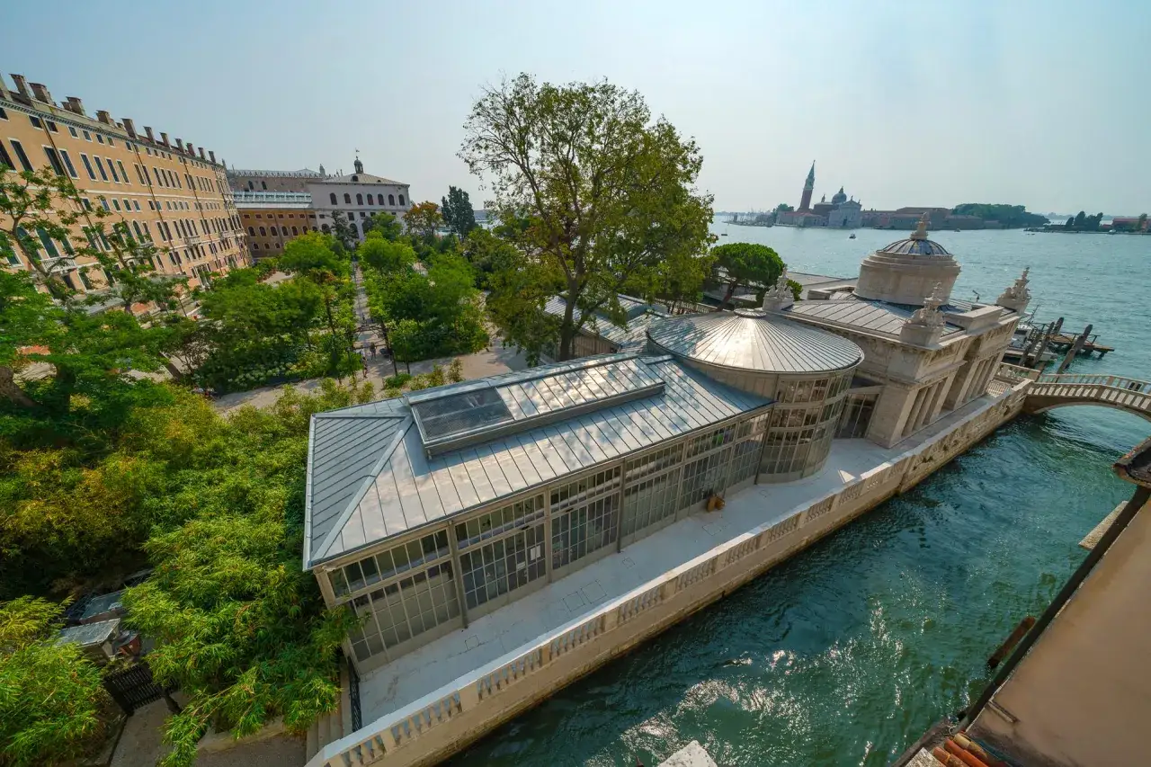 Un angolo di pace tra i giardini di Venezia, con un edificio moderno affacciato sul canale e sullo sfondo l'isola di San Giorgio Maggiore.