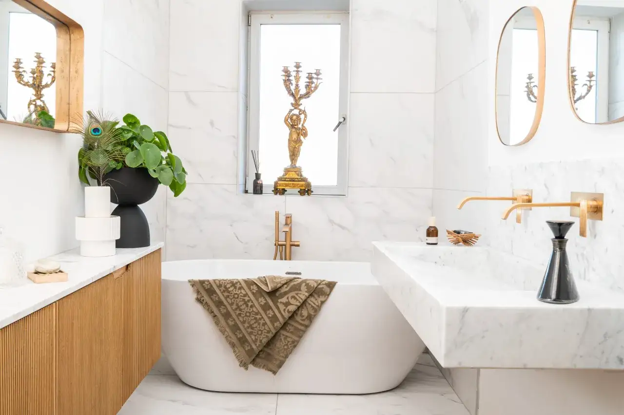 Aménagement salle de bain moderne avec baignoire îlot, lavabo en marbre, robinetterie dorée et décoration élégante.