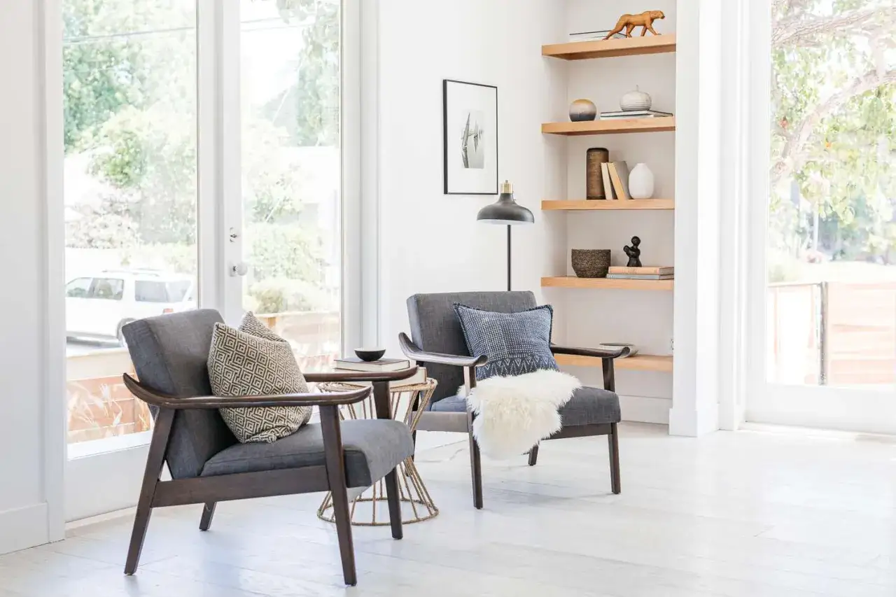 A corner cozy reading nook with two grey armchairs, decorative pillows, a side table, and a floor lamp.