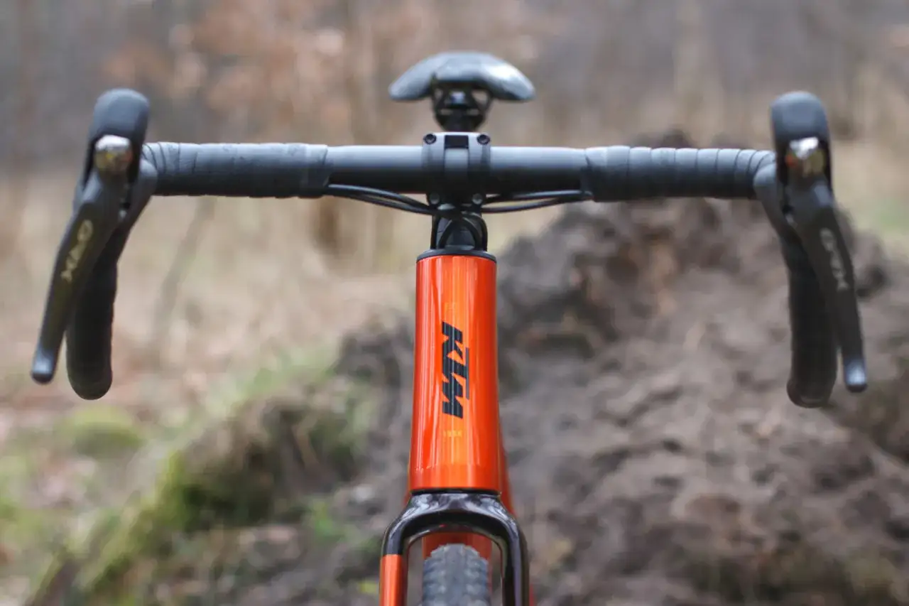 Pomarańczowy rower KTM z kierownicą typu gravel. Idealny na szutrowe trasy, bo gravel to wszechstronność.