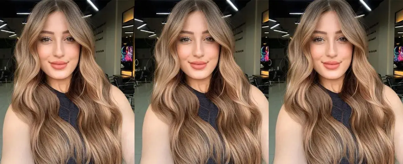 Mujer con cabello largo y ondulado, con un degradado de color que va de castaño a rubio. Un ejemplo perfecto de cómo aclarar el pelo para un look natural.
