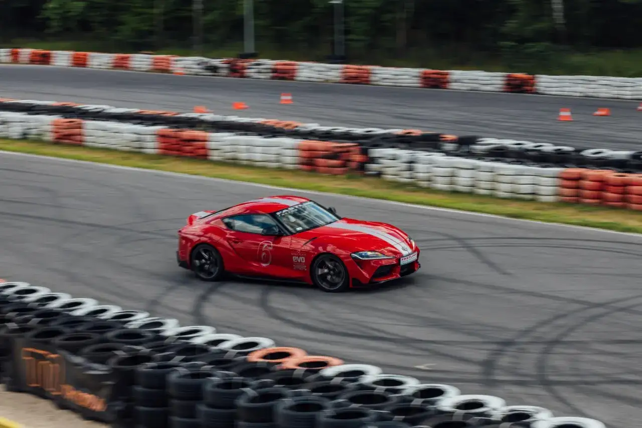 Czerwona Toyota GR Supra z białymi pasami pędzi po torze wyścigowym, zostawiając za sobą ślady opon.