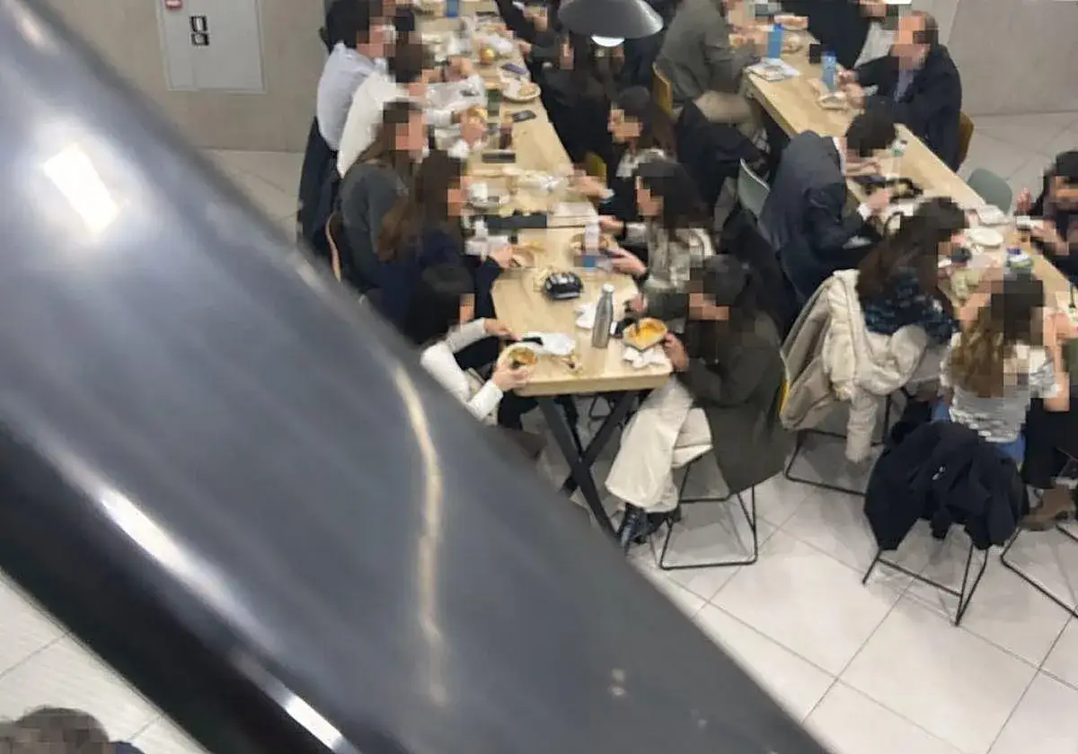Personas disfrutan tiempo para comer en el trabajo, sentados en mesas largas con comida y bebidas.