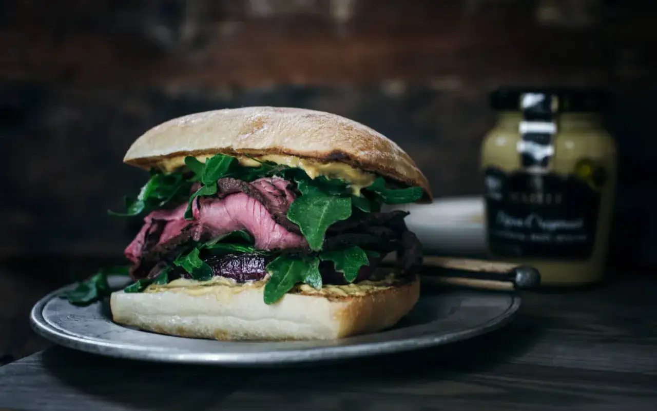 En saftig steak sandwich med rosastekt kött, ruccola och senap på en rustik tallrik.