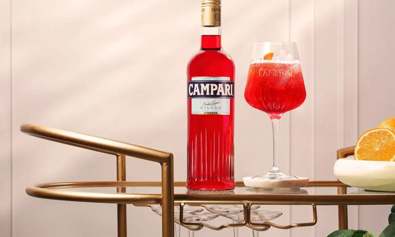Elegancki drink z campari, podany w kieliszku z lodem i plasterkiem pomarańczy, obok butelki tego samego alkoholu.