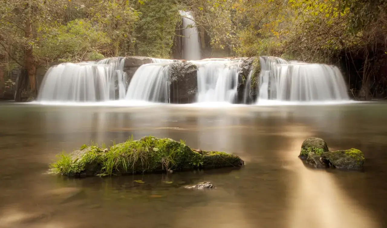 Cascata nella valle del Treja, con rocce ricoperte di muschio e vegetazione lussureggiante. L'acqua scorre dolcemente creando un effetto setoso.