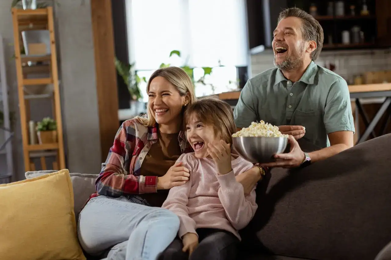 Rodzina śmieje się podczas oglądania filmów dla całej rodziny, jedząc popcorn z dużej miski.