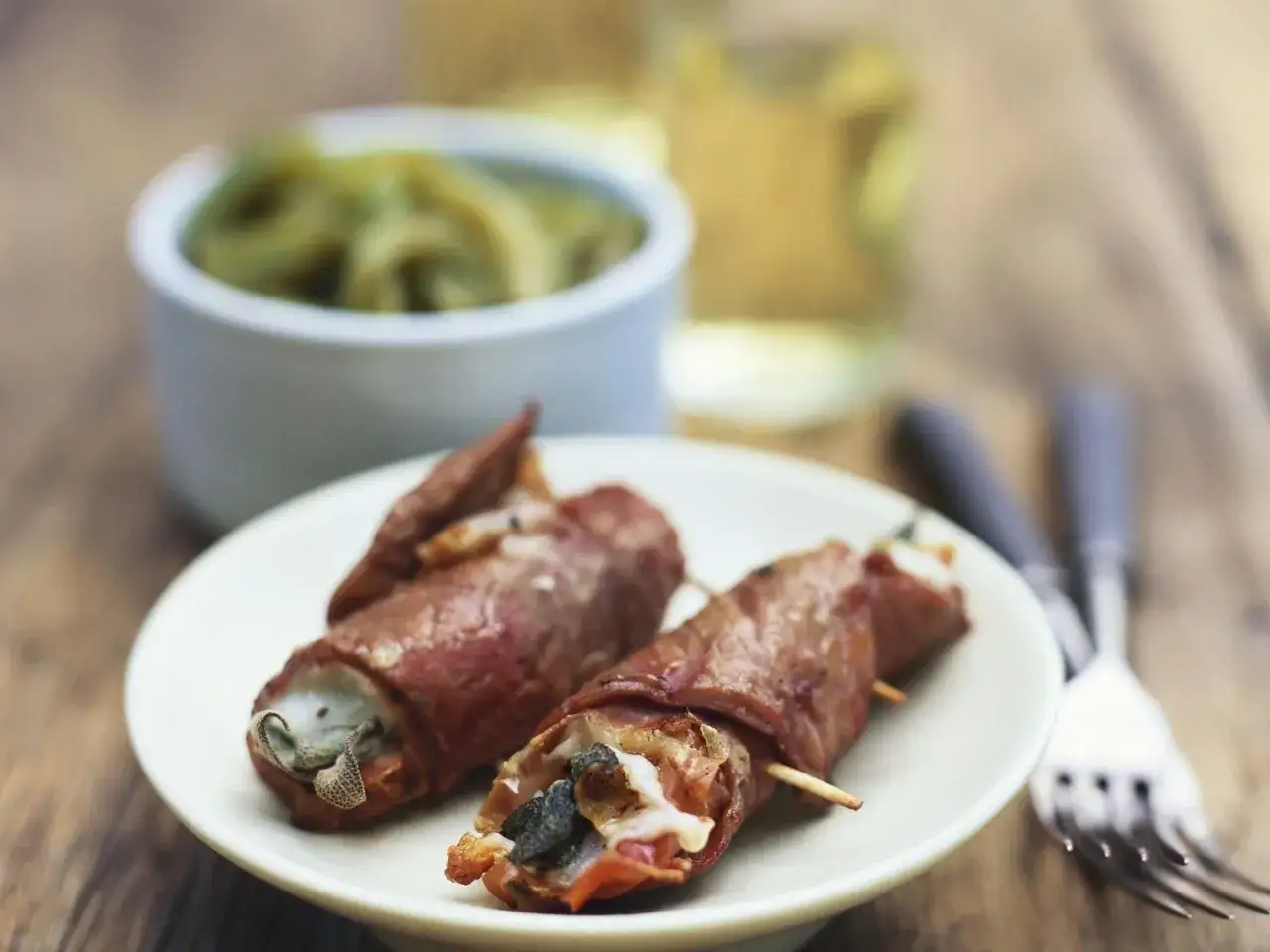 Zwei Involtini auf einem Teller, umwickelt mit Speck und gefüllt mit Salbei. Ein authentisches Involtini-Originalrezept, bereit zum Genuss.