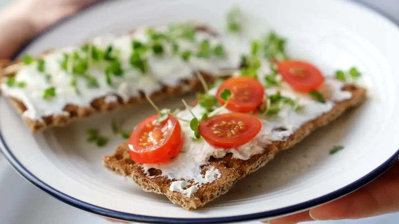 Tostadas integrales con queso tofu cremoso, rodajas de tomate cherry y brotes verdes frescos.