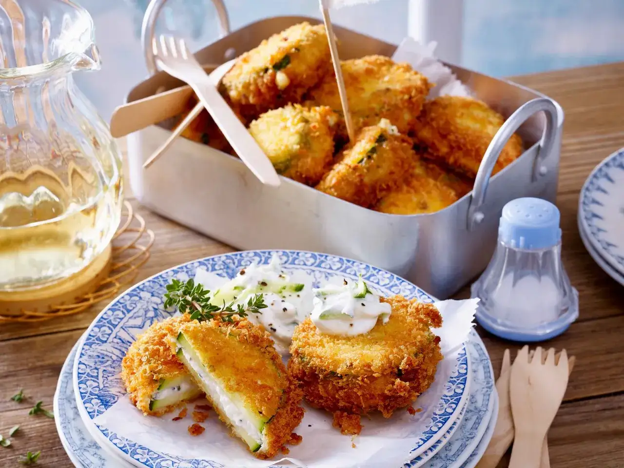 Knusprig panierte Zucchini-Scheiben, gefüllt mit Frischkäse, serviert mit Dip und Kräutern. Ein Genuss!