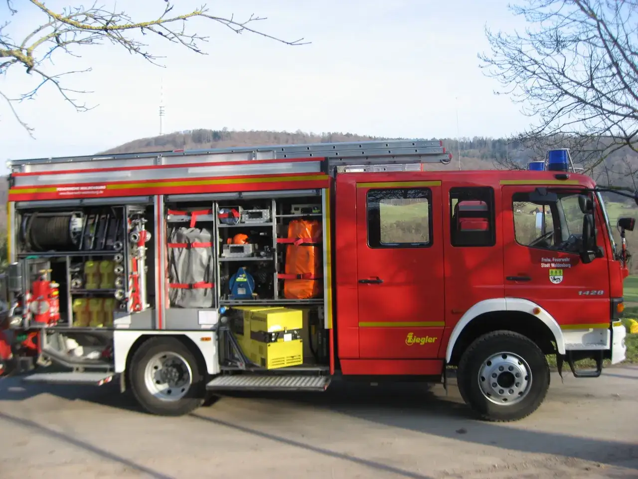 Rotes Feuerwehrauto mit vielen Geräten, wie Schläuche und Leitern, bereit für den Einsatz nach DIN 14530-5.