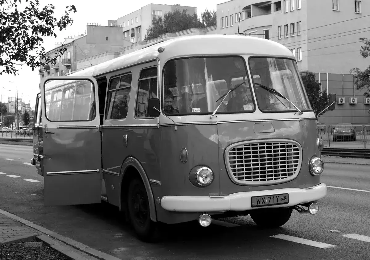 Stary autobus, jak wituś marynarz, czeka na pasażer&oacute;w. Drzwi otwarte, kierowca w okularach patrzy przed siebie.