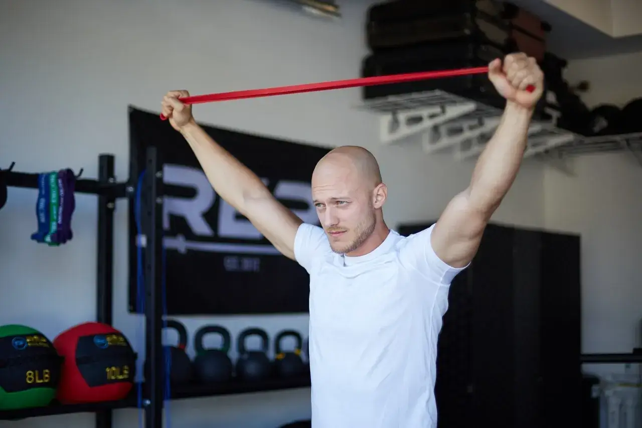 Mężczyzna wykonuje ćwiczenia na biceps w domu z czerwoną gumą oporową.