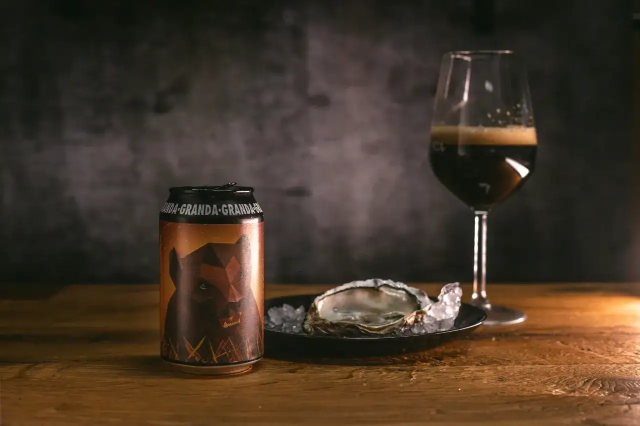 Lattina di oyster stout con ostrica su ghiaccio e bicchiere di birra scura.