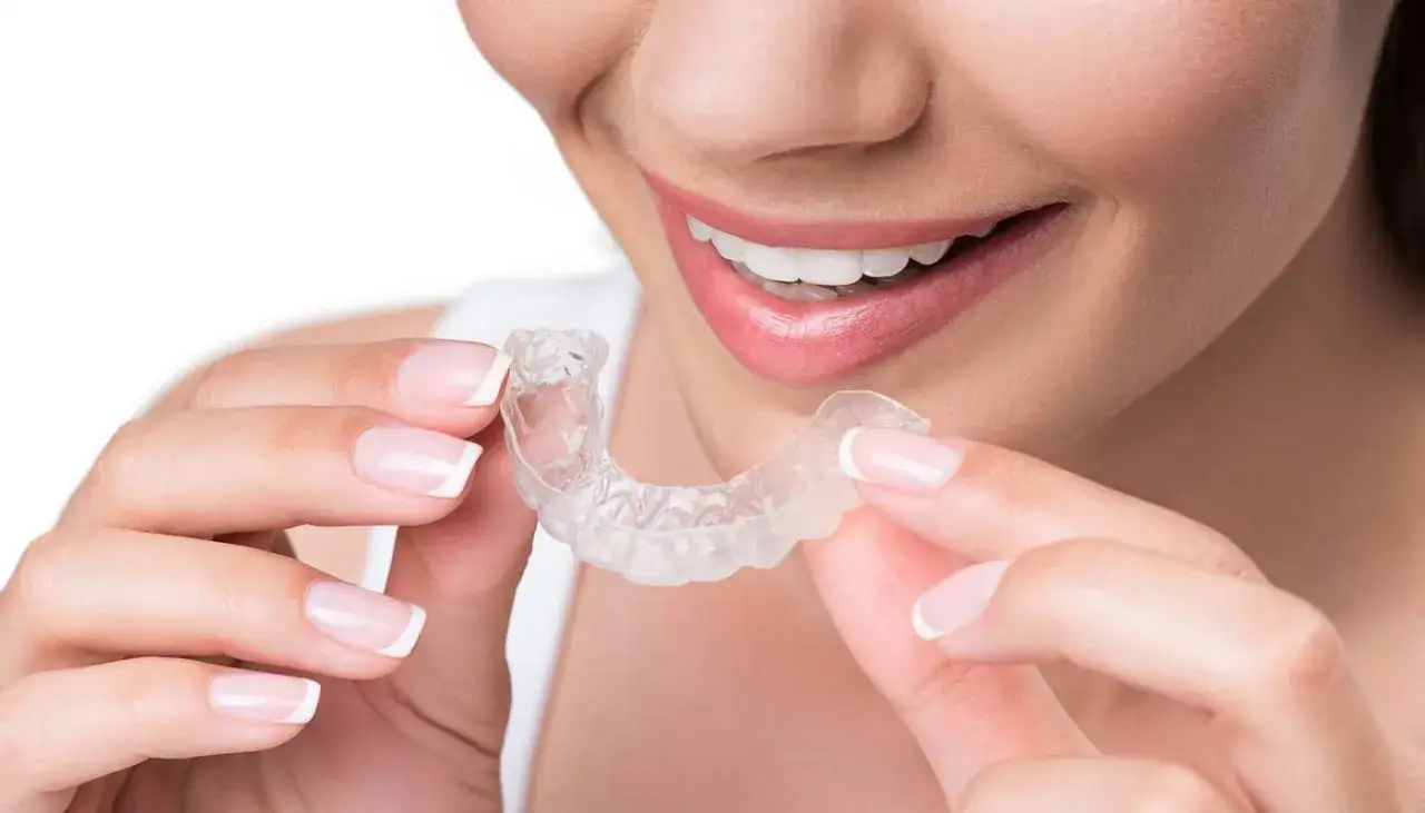 Donna sorridente mostra un bite apparecchio trasparente, tenuto tra le dita con unghie curate.