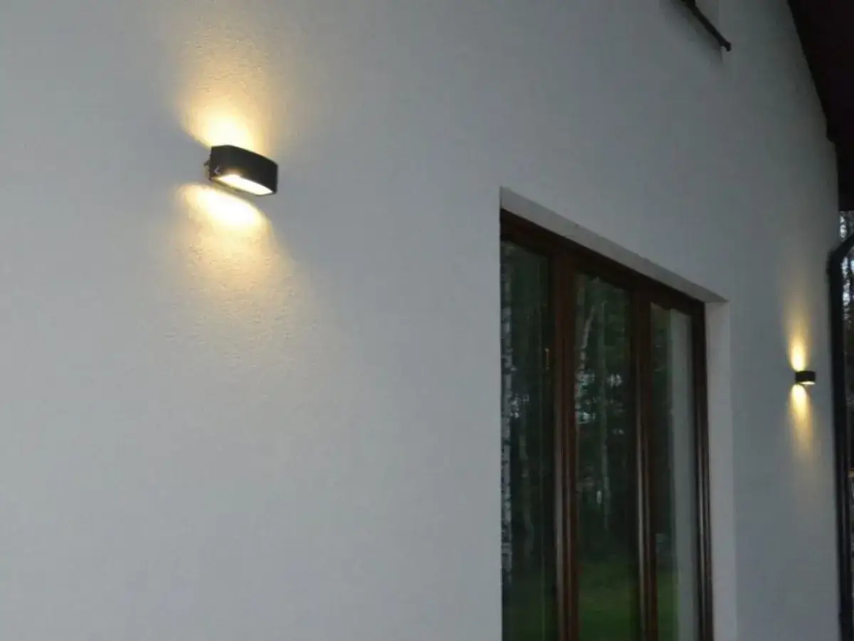 Nierówności na elewacji pod światło, tworzące ciekawe cienie. Dwa kinkietowe punkty świetlne oświetlają ścianę domu.