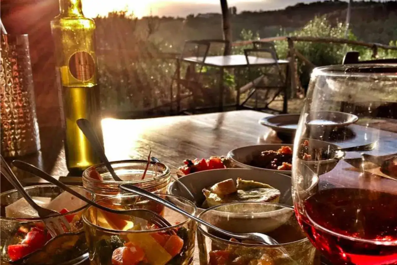 Un delizioso **weekend in Toscana**: antipasti, vino rosso e tramonto su un tavolo all'aperto.
