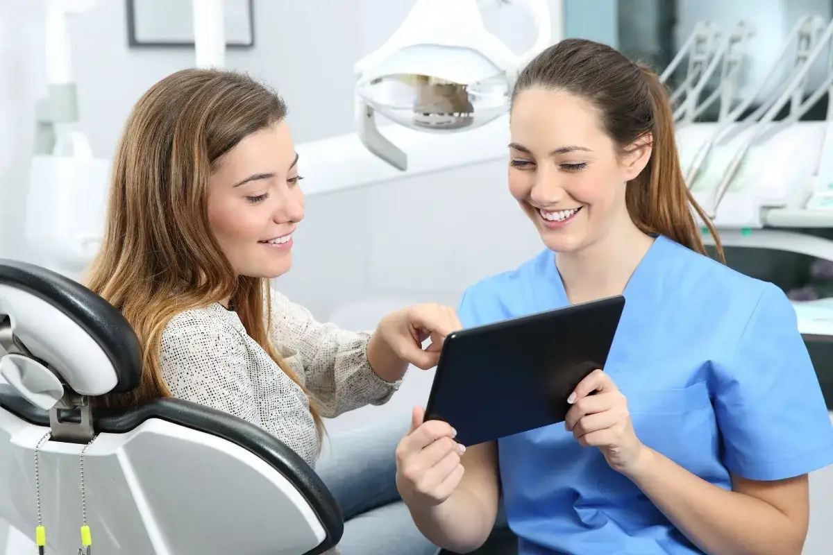 Uśmiechnięta dentystka pokazuje pacjentce tablet. Nawet jeśli boje się dentysty, jej spokój i profesjonalizm budzą zaufanie.