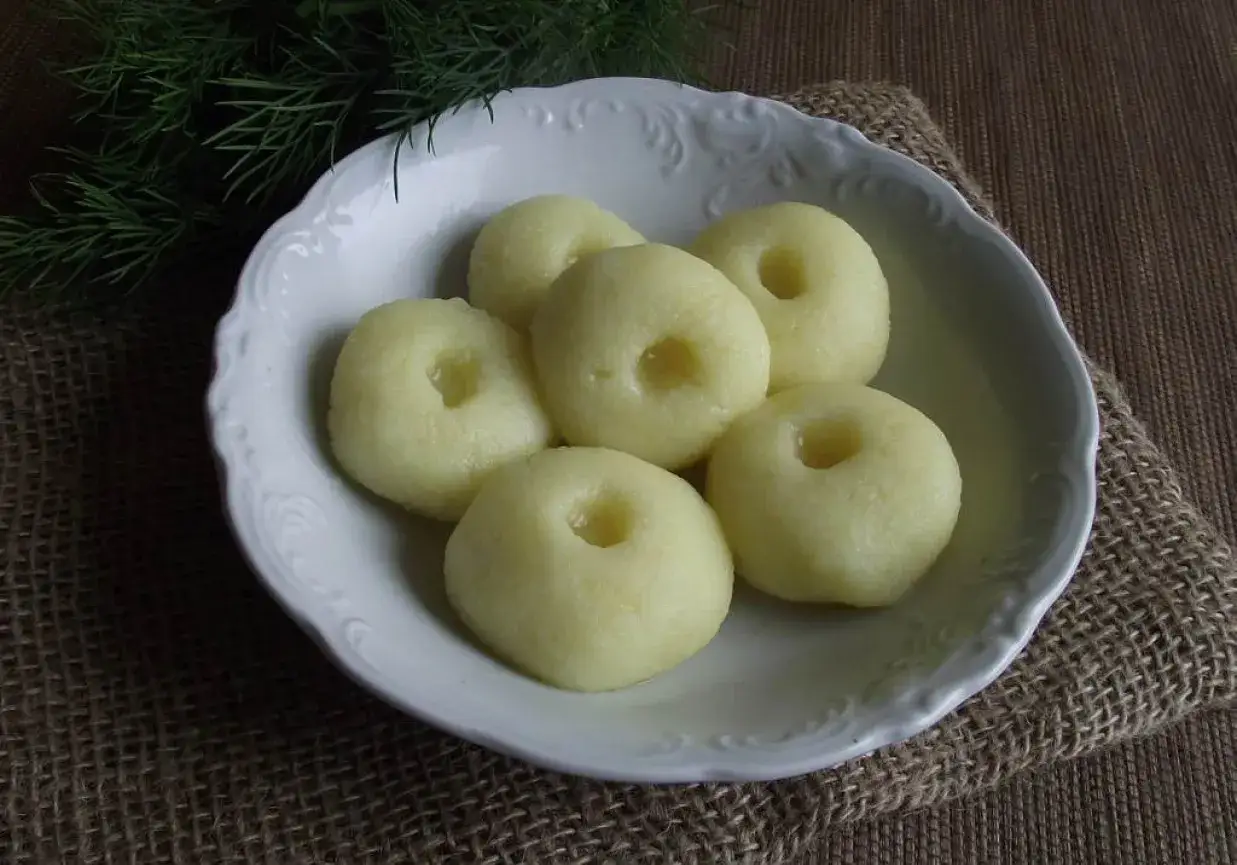 Kluski śląskie bez jajka, delikatne i puszyste, podane w białej miseczce z zielonym koperkiem.