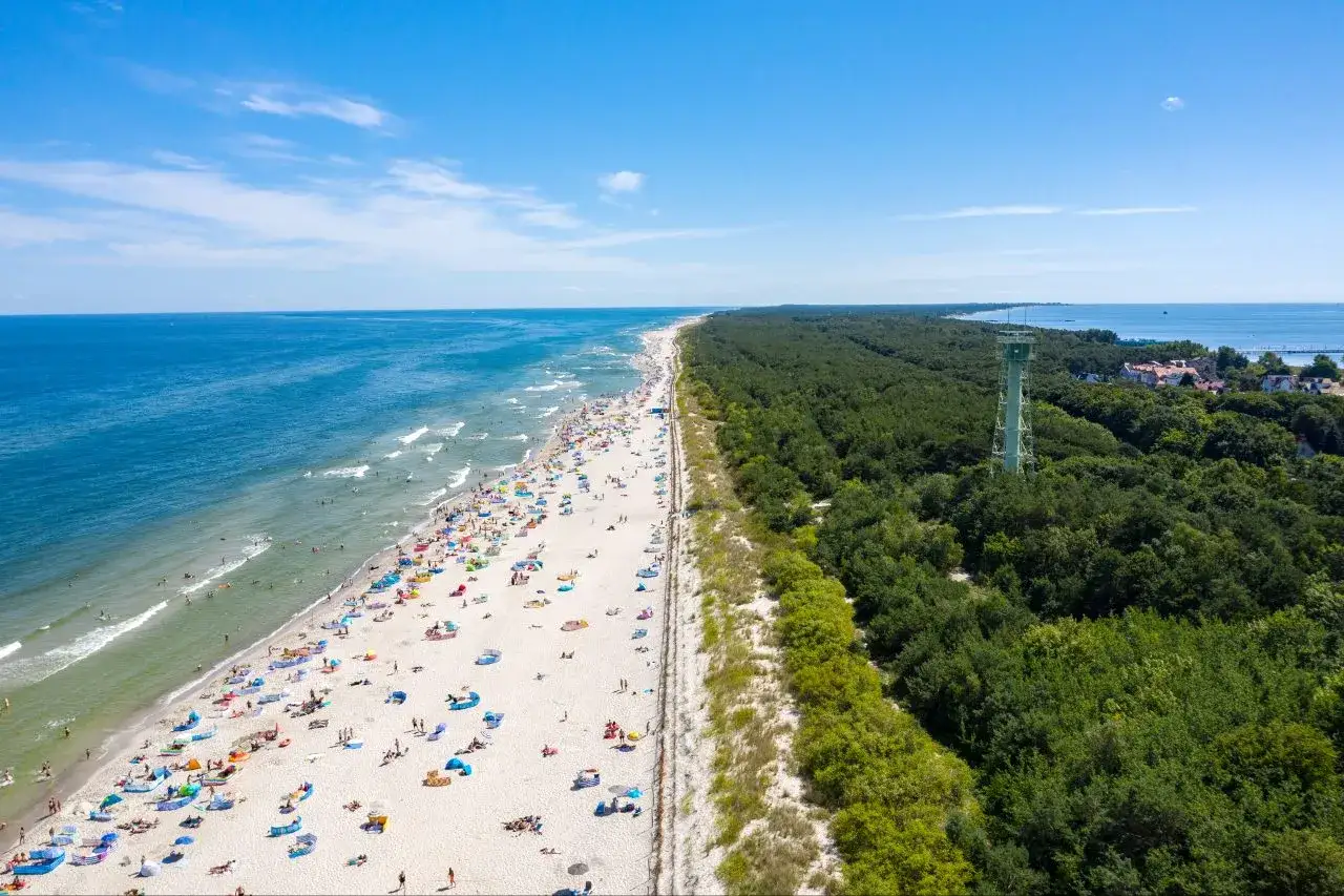 Słoneczna plaża pełna ludzi, las i wieża widokowa – idealne pomorskie atrakcje na weekend.