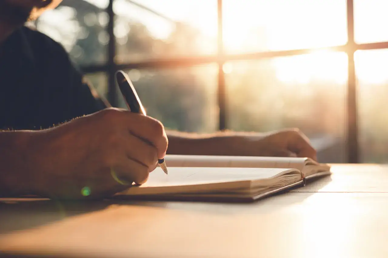 A person's hands writing in a journal, bathed in warm sunlight. This scene evokes a sense of introspection and the journey of self discovery questions.