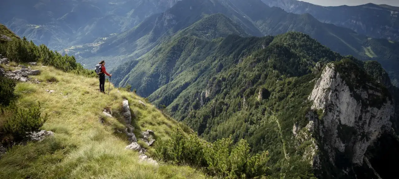 Escursionista ammira il panorama mozzafiato dal **Monte Zugna**, circondato da verdi montagne e valli profonde.
