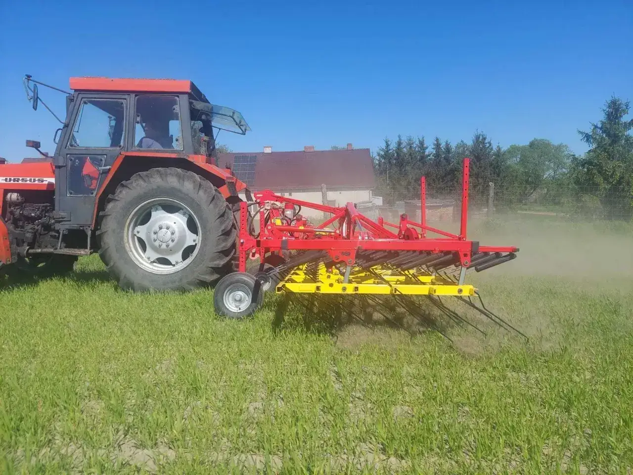 Czerwony traktor Ursus z agregatem uprawowym, który działa jak buster, spulchnia ziemię na polu.