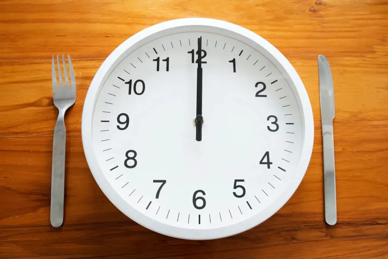 Uhr zeigt 12 Uhr. Gabel und Messer liegen bereit. Zeit für die Mittagspause während der Arbeitszeit.