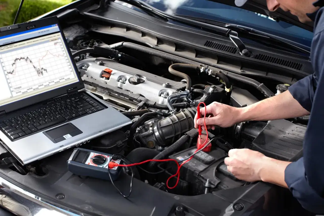Mechanik sprawdza parametry silnika przy użyciu laptopa i multimetru, przygotowując auto do wypalania DPF na postoju.