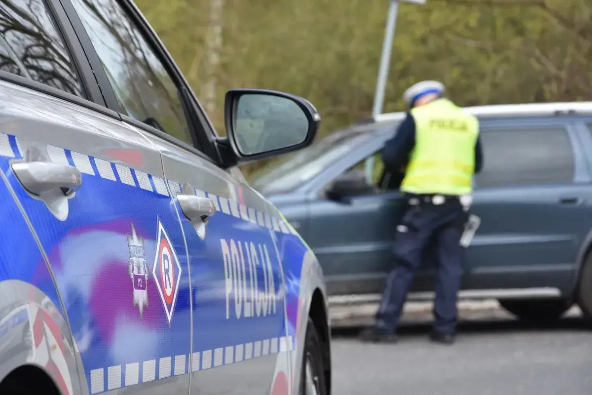Policjant w kamizelce odblaskowej kontroluje dokumenty kierowcy. Pamiętaj, jakie dokumenty musi mieć kierowca samochodu osobowego, by uniknąć mandatu.