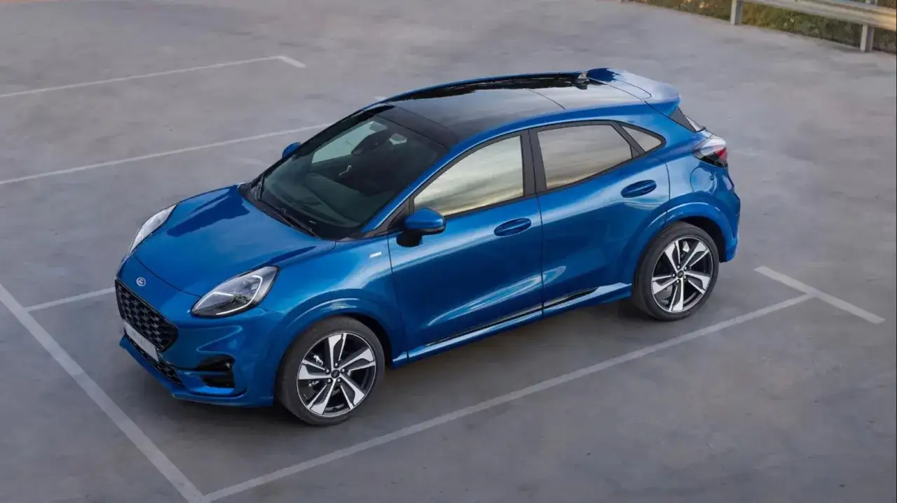 Błękitny Ford Puma, sportowy SUV, parkuje na betonowym placu. Jego lśniąca karoseria odbija niebo.