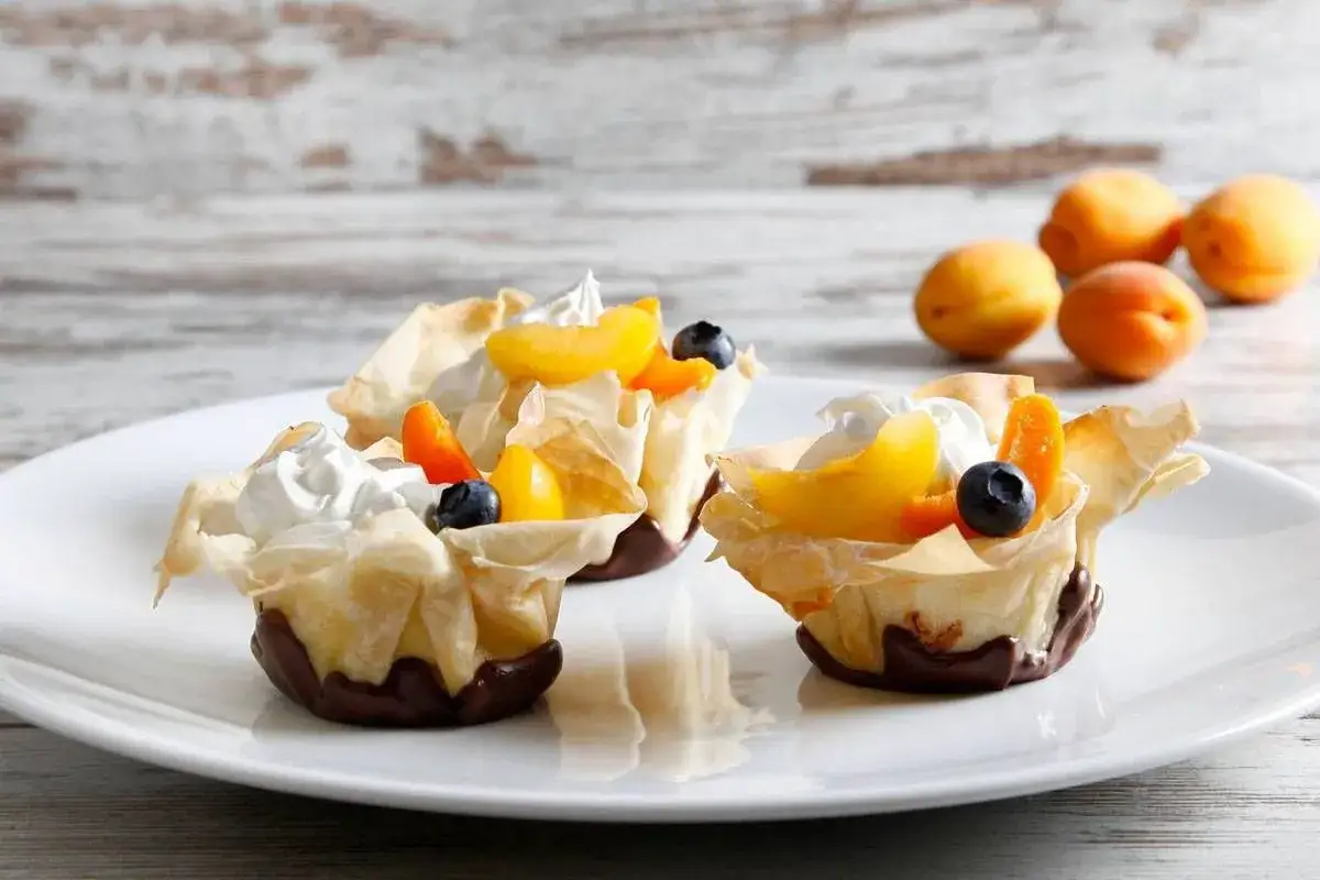 Deliziosi dolci con pasta fillo, ripieni di crema e guarniti con pesche, albicocche e mirtilli.