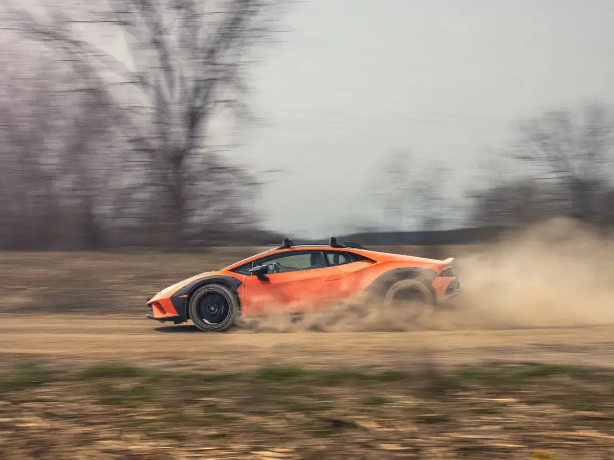 Pomarańczowy Lamborghini Sterrato szaleje po piaszczystej drodze, wzbijając tumany kurzu.