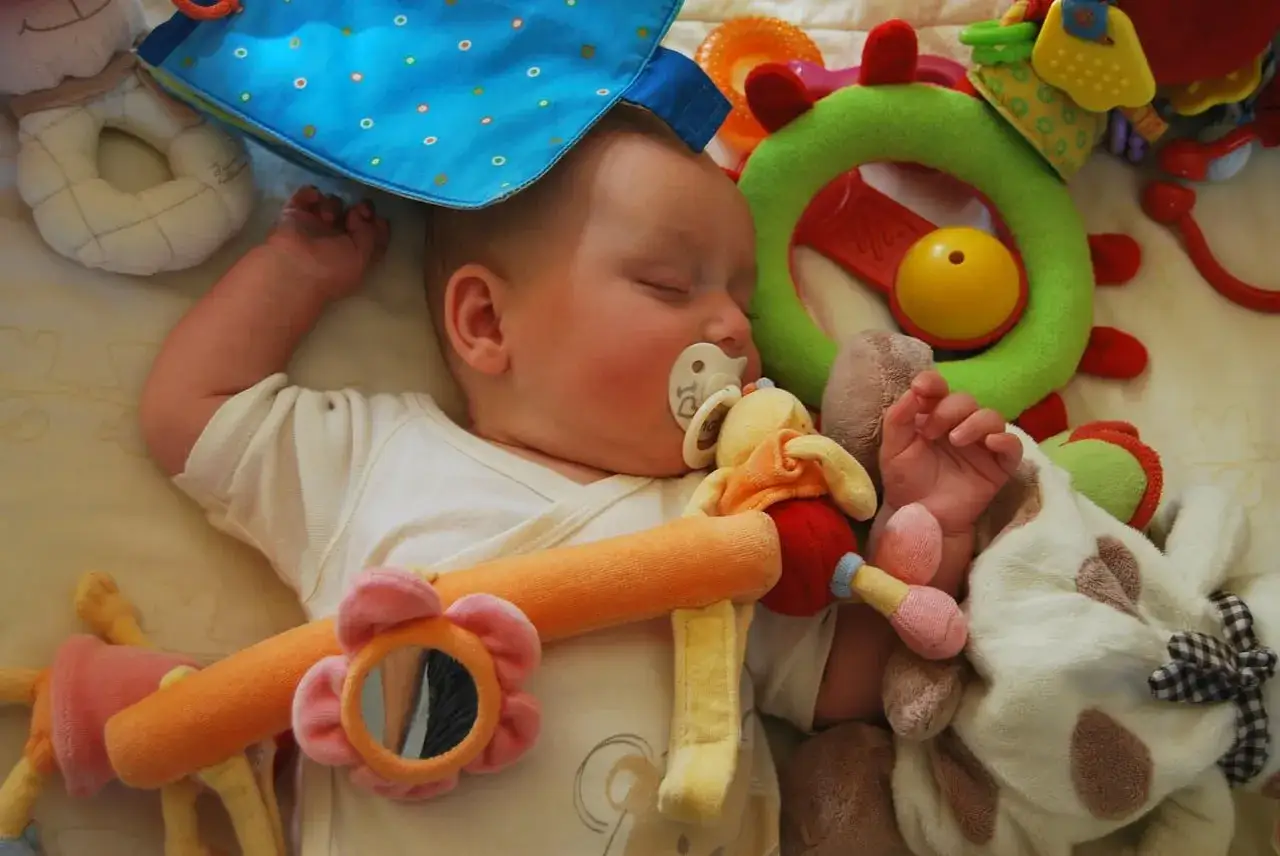 Schlafendes Baby mit Schnuller und Spielzeug. Ab wann Schnuller? Diese Frage stellen sich viele Eltern.