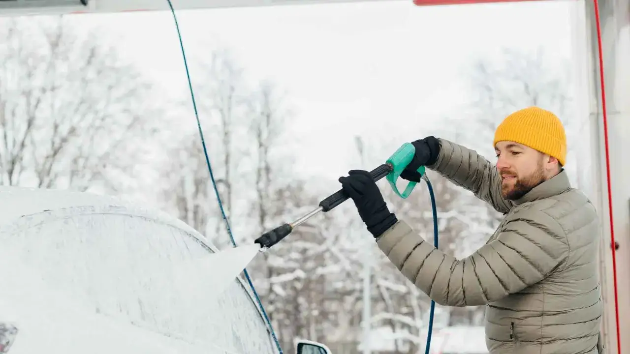 Man med gul m&ouml;ssa tv&auml;ttar bilen med h&ouml;gtryckstv&auml;tt i sn&ouml;igt v&auml;der. Underspolning bil f&ouml;r att f&aring; bort vintersmuts.