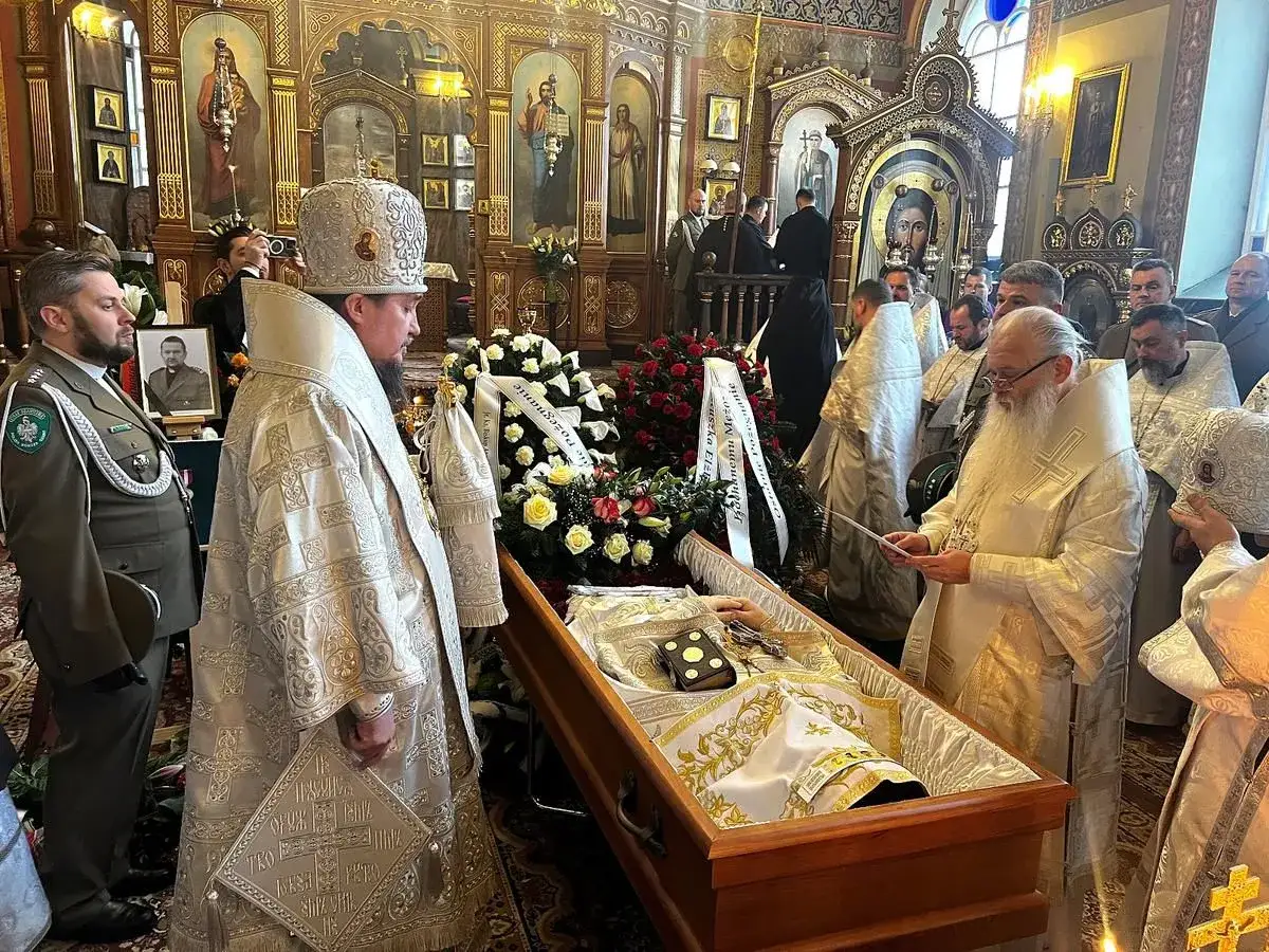 Uroczystość pogrzebowa w cerkwi. Duchowni w bogatych szatach modlą się przy trumnie.