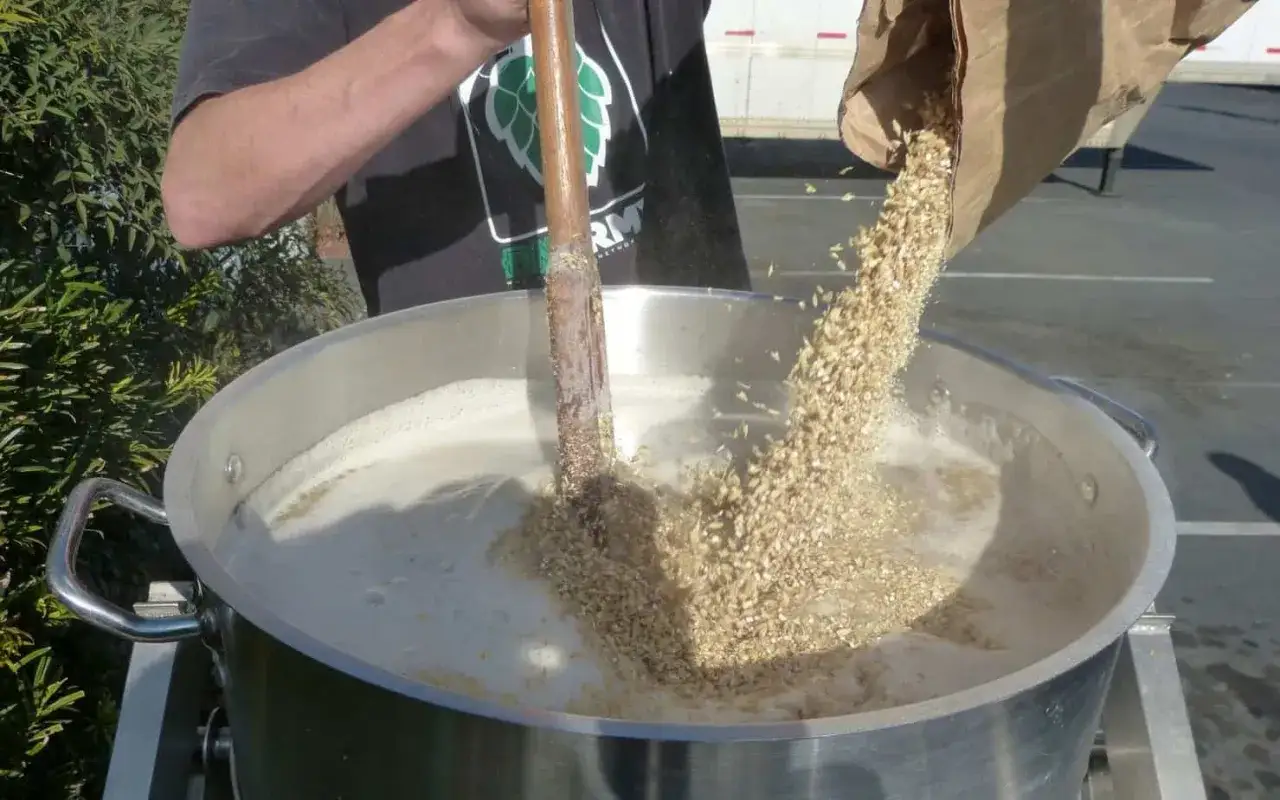 Un birraio aggiunge chicchi di malto in una pentola per preparare una birra al mais.