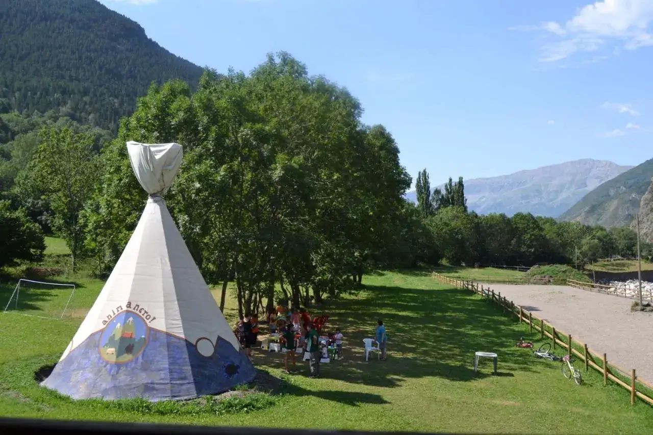 Tienda tipi decorada en un camping en Huesca, rodeada de árboles y montañas. Niños jugando cerca.