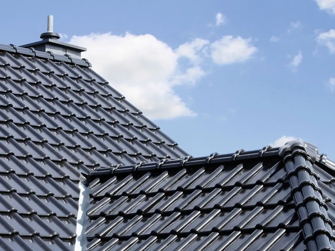 Nowy dach z czarnej dachówki ceramicznej, jakby zrobiony z połyskującego roben piemont, lśni w słońcu.