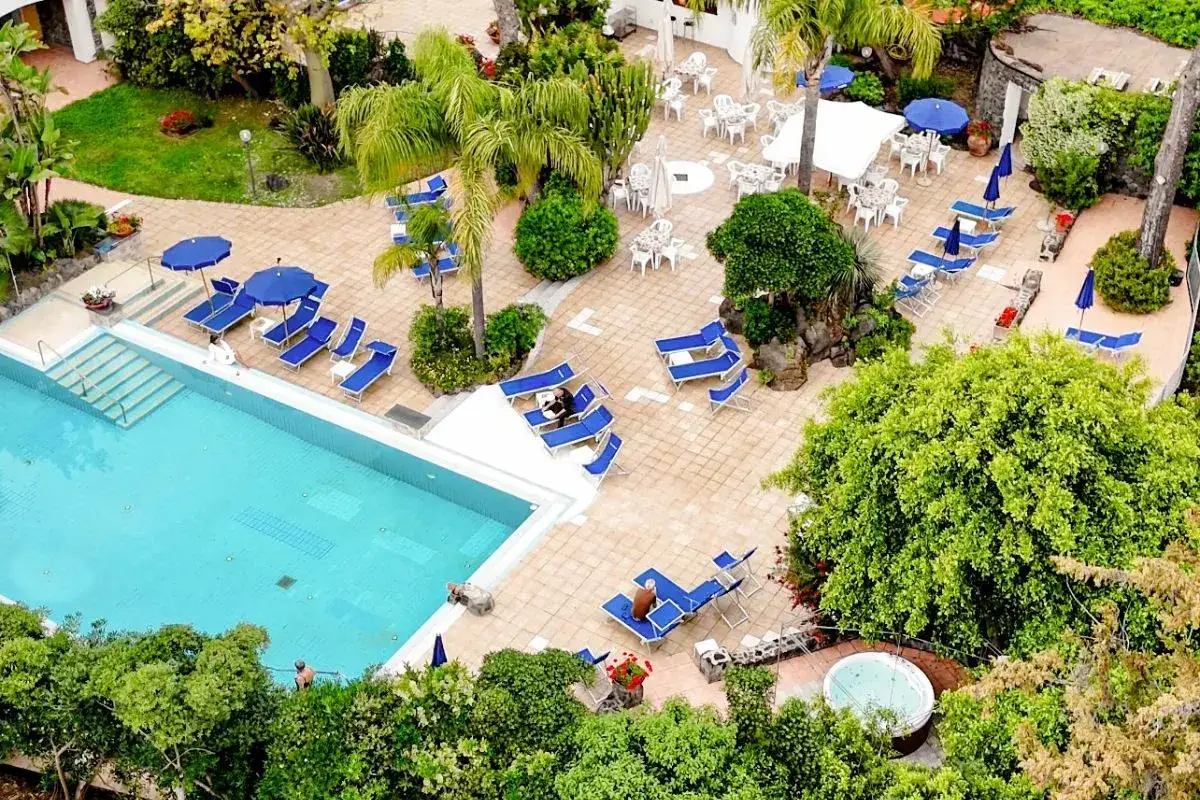 Piscina e lettini prendisole al **hotel San Giovanni Ischia**, circondati da vegetazione lussureggiante e un'area con tavoli all'aperto.