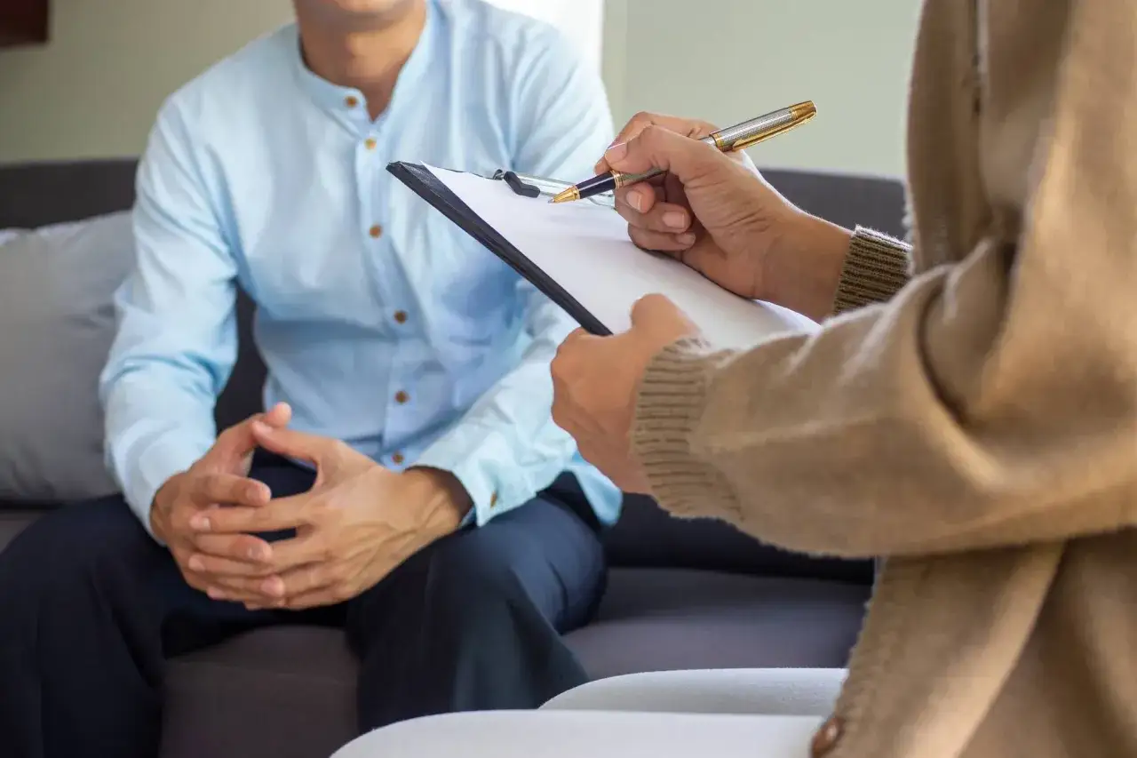 Wizyta u psychiatry. Pacjent siedzi na kanapie, a terapeuta notuje na kartce.