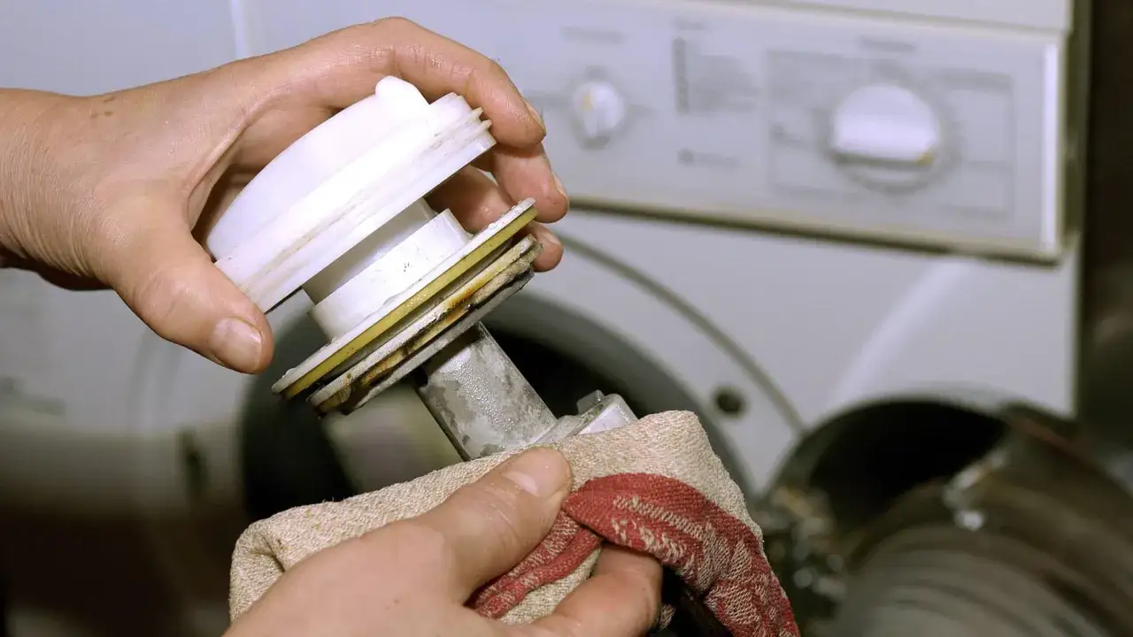 H&auml;nde reinigen den verschmutzten Waschmaschinenfilter mit einem Tuch. Regelm&auml;&szlig;iges Waschmaschinen Filter Reinigen verhindert Sch&auml;den.