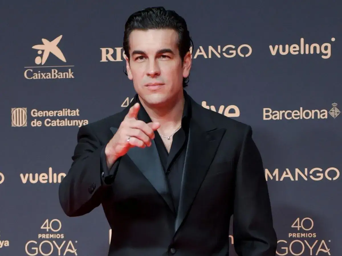 Mario Casas posa con un traje negro en la alfombra roja de los Premios Goya, se&ntilde;alando a la c&aacute;mara.