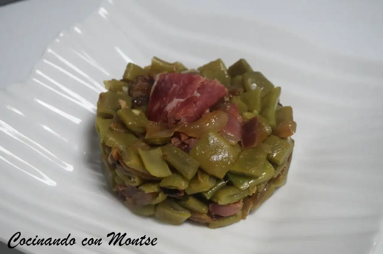 Jud&iacute;as verdes con jam&oacute;n, un plato sencillo y sabroso, presentado en un mont&iacute;culo sobre un plato blanco.