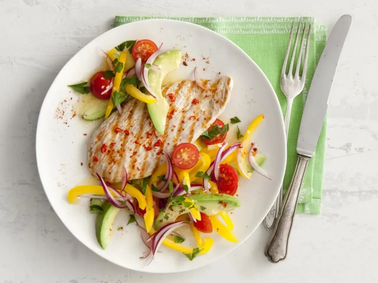 Gegrilltes Putenfleisch marinieren mit einem bunten Salat aus Avocado, Tomaten, Paprika und Zwiebeln. Gewürzt mit Chili und Petersilie.